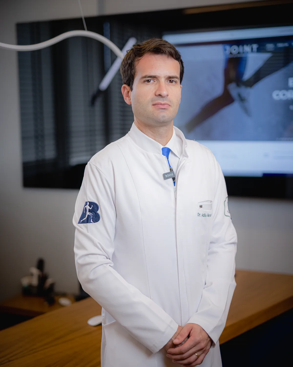 Dr. Adílio Bernardes de jaleco no consultório da Clínica JOINT