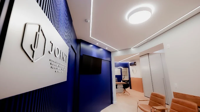 Circulação da Clínica JOINT, com logotipo em relevo e sala de espera ao fundo