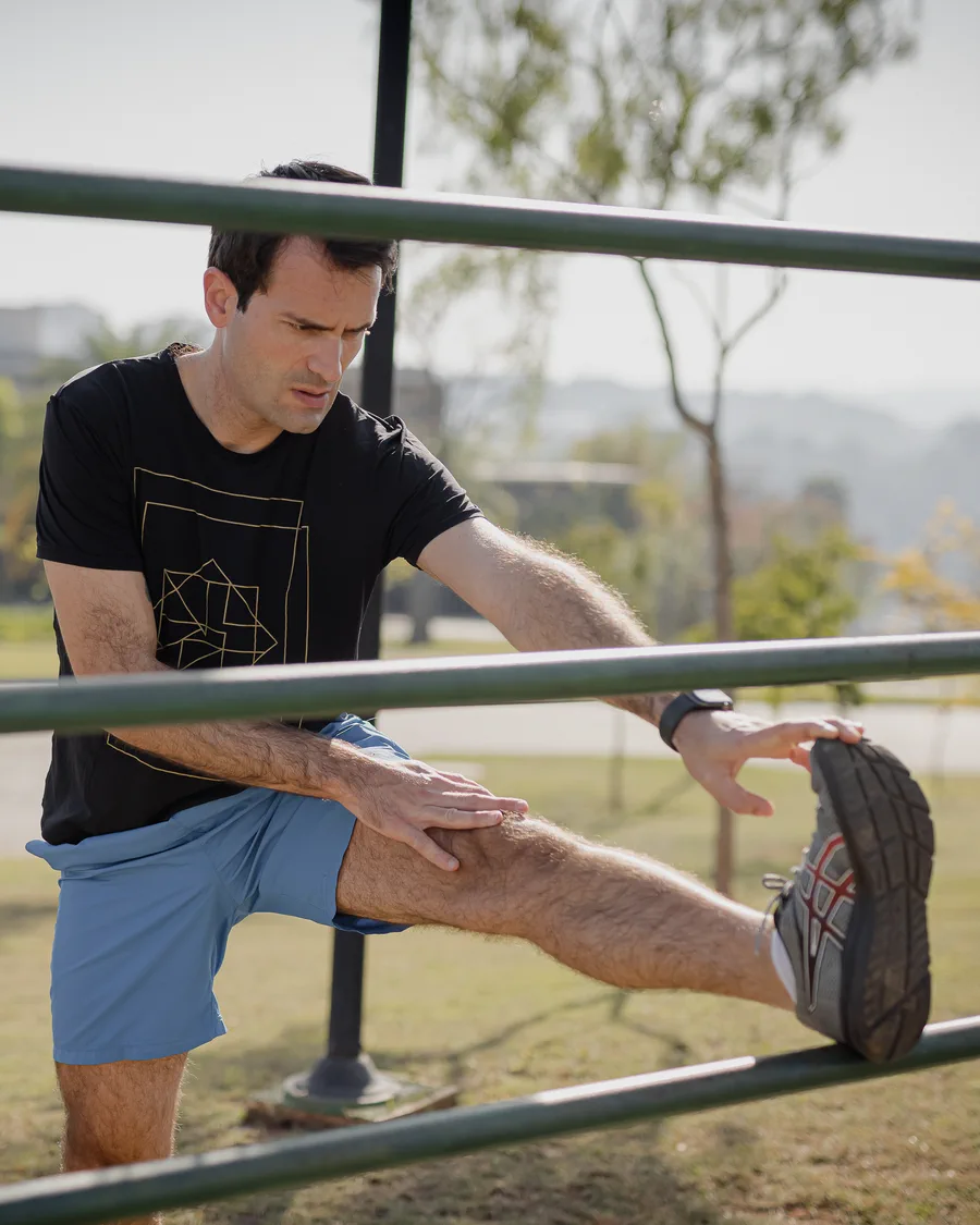 Homem alongando o joelho apoiado em barra de exercício ao ar livre